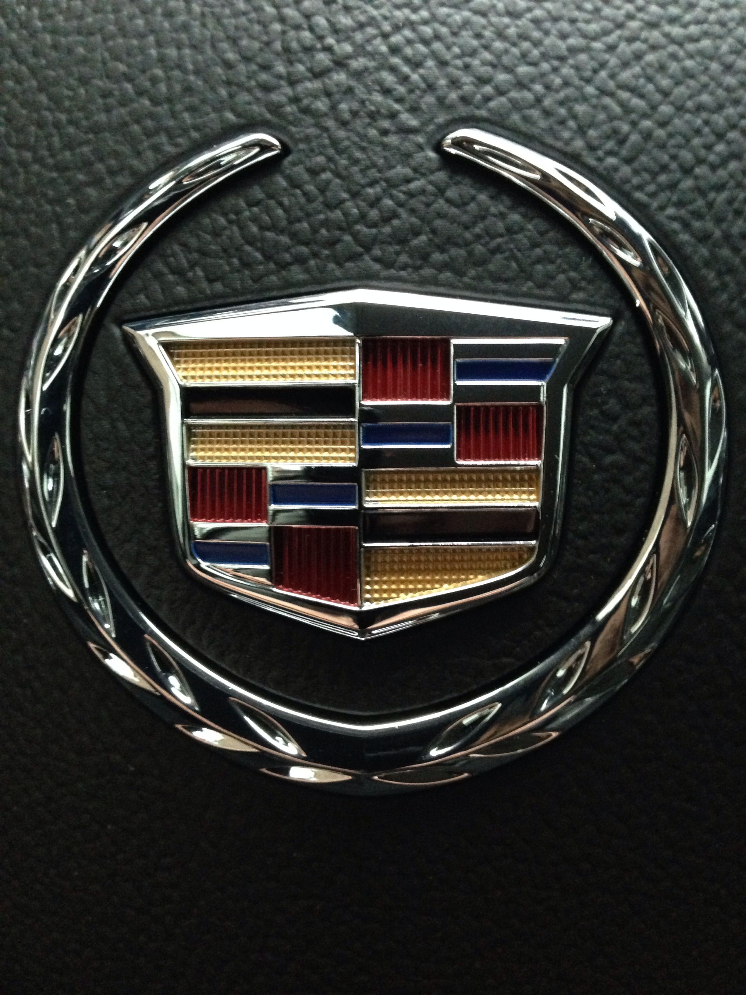 Круглые знаки машин. Значок Кадиллака и Джилли. Знак Кадиллак Эскалейд. Cadillac Escalade марка. Знак Кадиллака на машине.